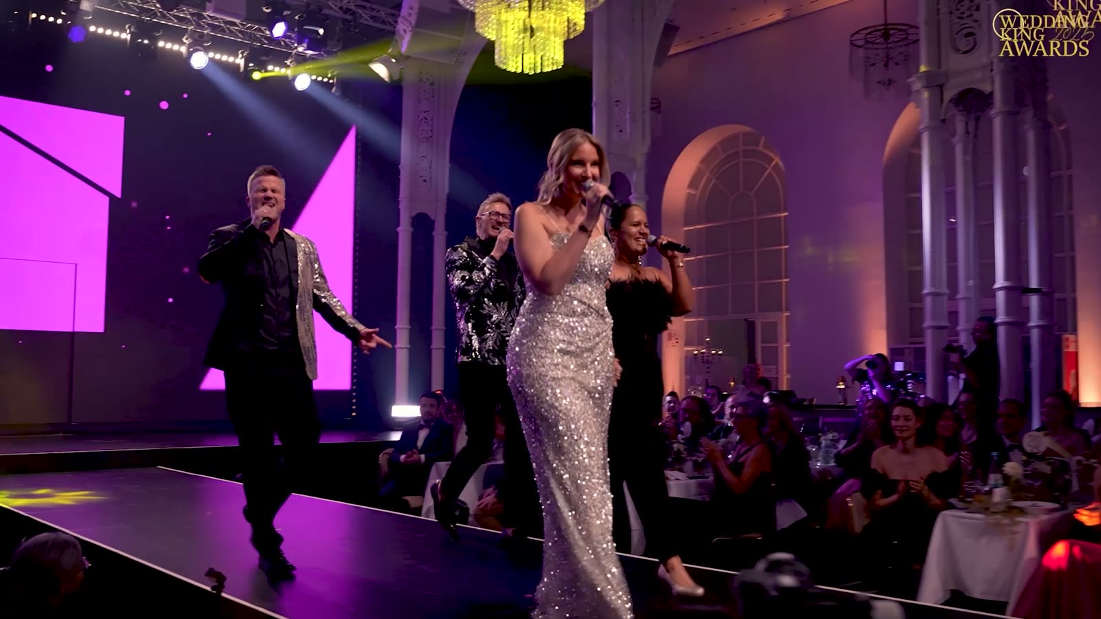 Fünf Acts singen gemeinsam auf dem Laufsteg der Flora Köln, rechts das Publikum an festlich gedeckten Tischen